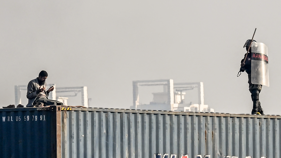 A man is seen praying on top of a shipping container as a paramilitary soldier approaches him during a protest demanding the release of former prime minister Imran Khan, at the Red Zone area in Islamabad on November 26, 2024. 