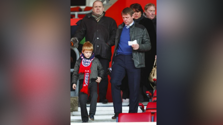 Stuart Pierce is walking down the stands with his son, Harley, who is wearing an England scarf, while Stuart was the England interim manager.