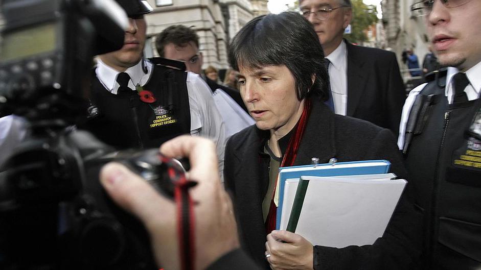 A younger looking Cressida Dick outside the Old Bailey in London flanked by police officers in 2007. She is carrying a pile of papers and a photographer is in the foreground taking a photo of her. 