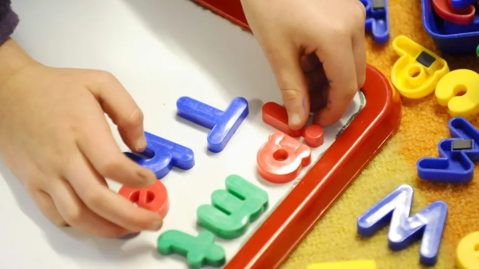 Two hands playing with toy multi-coloured letters on a whiteboard