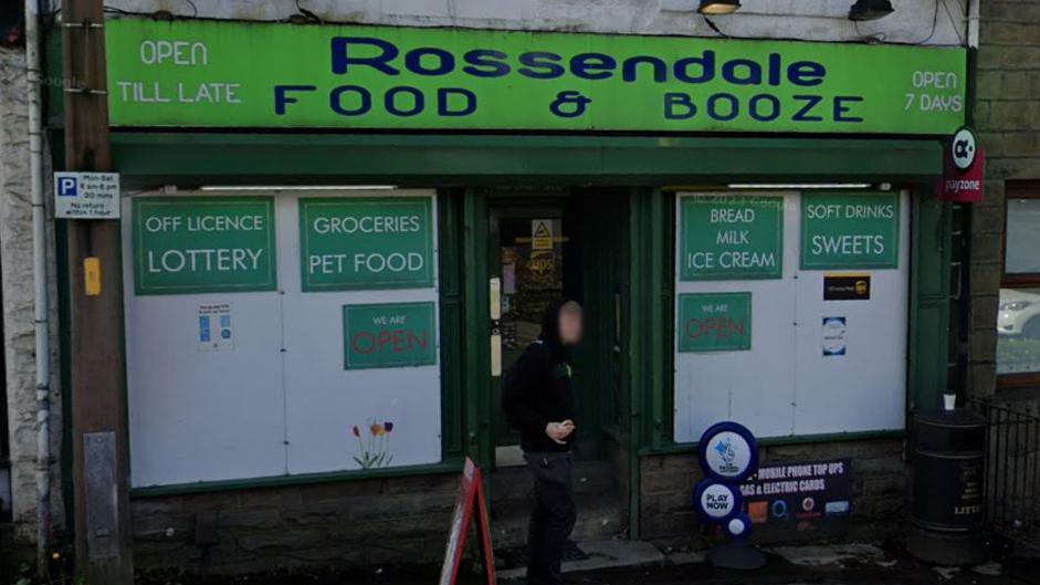 Street view image of Rossendale Food & Booze, a shop with a green sign and boarded up windows advertising food and groceries