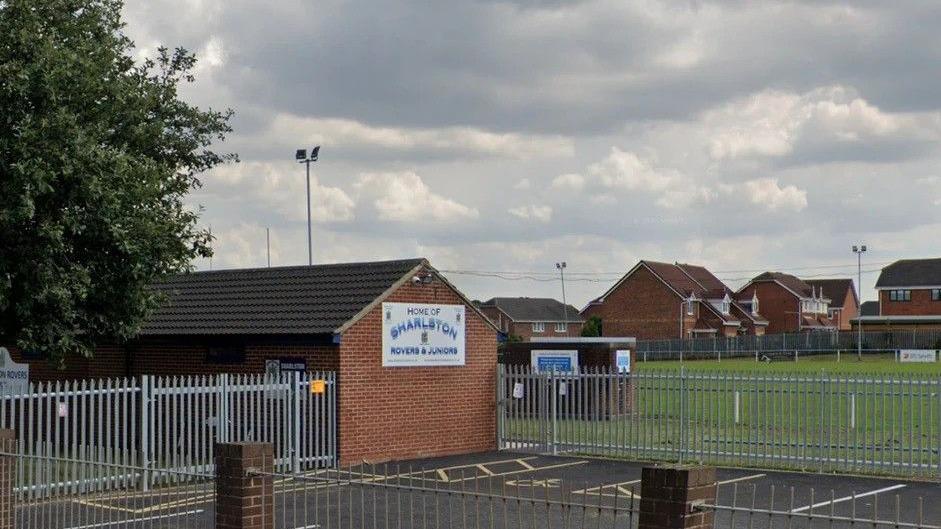 The outside of a rugby clubhouse surrounded by metal gates and a sports pitch in the background.