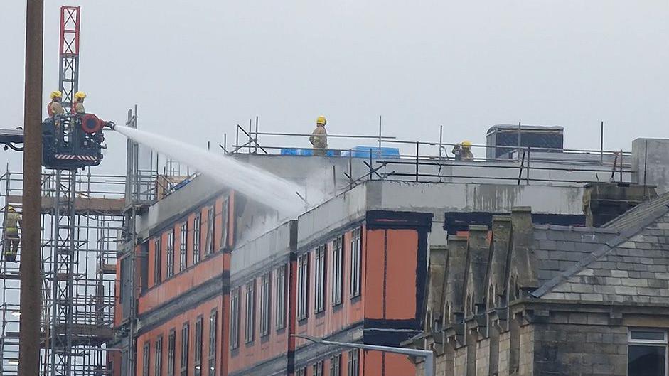 Firefighters on an aerial platform use water pumps to put out a blaze at the top of a block of flats under construction in Lancaster