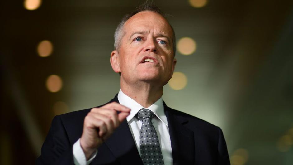 A middle aged man in suit and tie gestures with his hand as he speaks