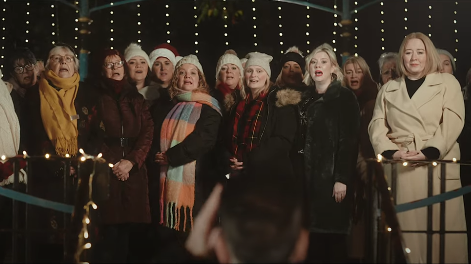 A large group of female carol singers standing and performing in a variety of winter attire.