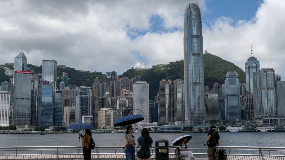 People are standing at Tsim Sha Tsui Promenade in front of the Hong Kong Skyline in Hong Kong