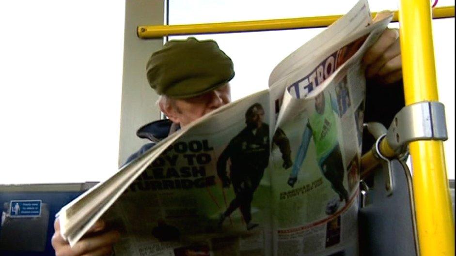 Man reading the paper on the bus