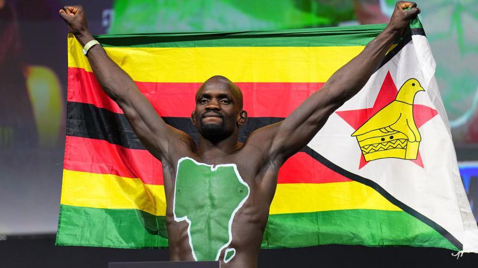 An athletic man with the outline of the African continent daubed on his torso in green holds up the Zimbabwe national flag above his head in Las Vegas, the US - Friday 6 December 2024