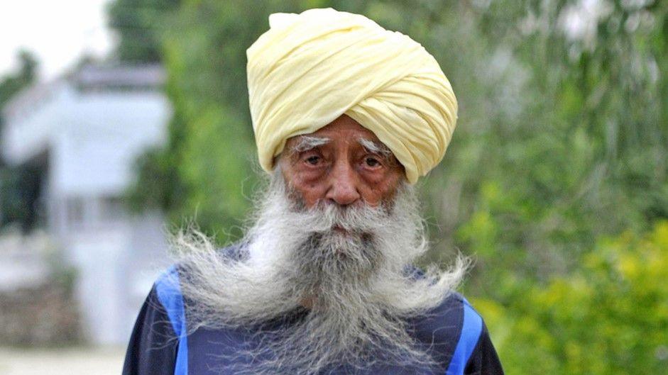 A man in a turban with a long grey beard looks at the camera