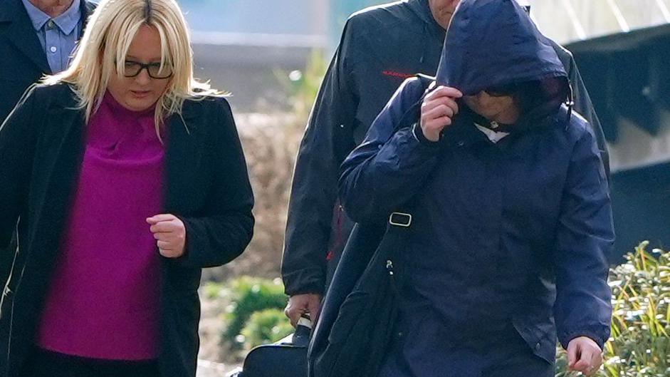 Joanne Sharkey, wearing a blue raincoat with the hood pulled up covering her face, arrives at court next to her solicitor dressed in a pink top and a blazer