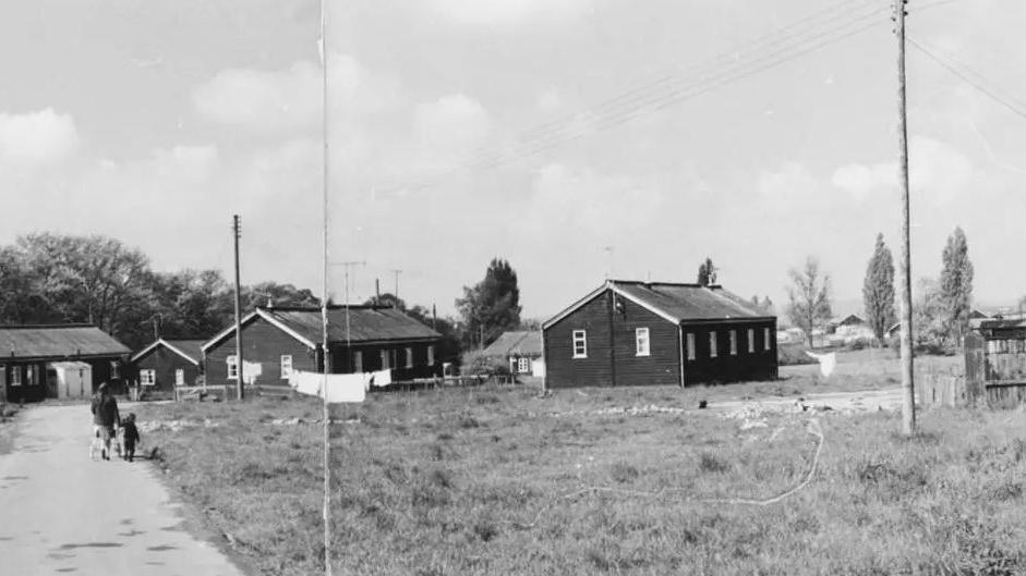 An archive black and white image from Slade Camp when residents still lived there. A mother and a child are walking towards the houses.