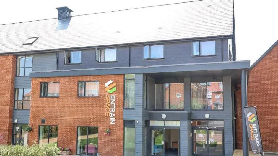 The Entrain building - a three-storey red-brick building with grey cladding and glass doors.