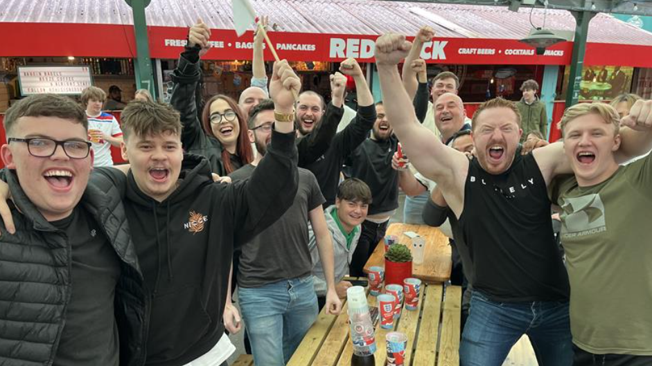 A large group of people all facing the camera, cheering and smiling, several of them are waving their fists in the air