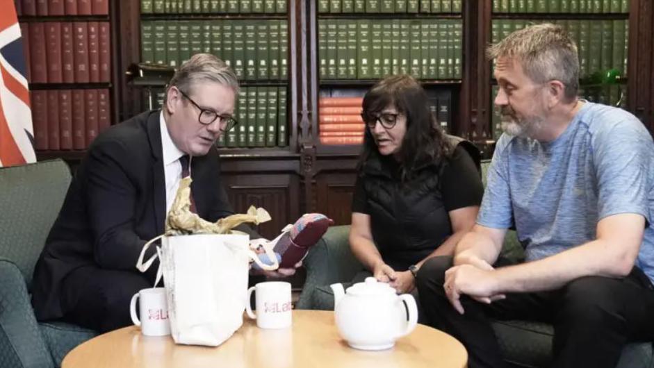 Prime Minister Keir Starmer (left) with Figen Murray (centre) and her husband Stuart sitting in a room with cabinets containing books