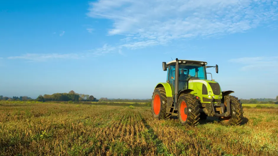 A lime green tractor with red and black wheels in a field. There is a blue sky with high white cloud. 