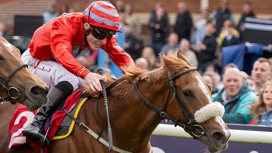 Jockey Rowan Scott dressed in red silks riding Boyne Lady to victory