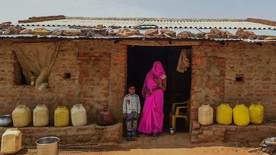 A woman in a bright pink saree with her head covered and a child wait for a government water tanker outside their house in Madhya Pradesh, India. Large parts of North India experienced a drought earlier this year.