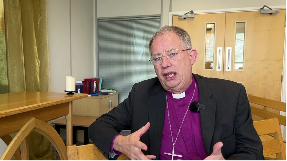 Dr Croft is pictured wearing a purple shirt and chain with a crucifix on it and a black jacket. He has short, grey hair and glasses.