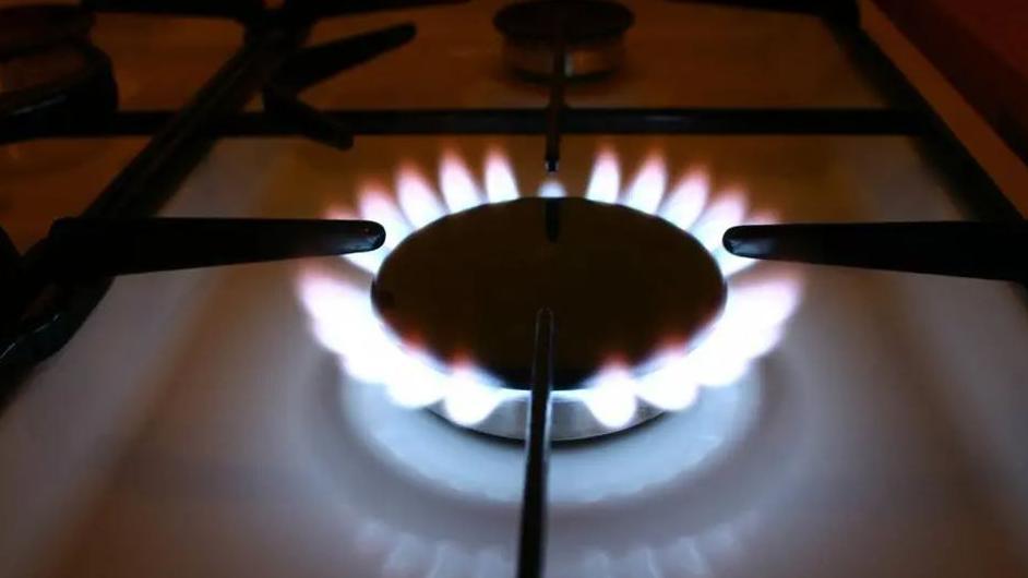 A close up of a lit gas ring on a white hob. The flames coming out of the dark ring are bright white with red tips.