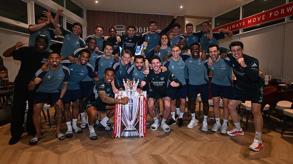 Arsenal players pose with a cutout of the Premier League trophy.