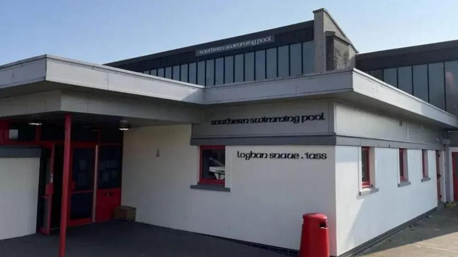 The outside of a white swimming pool building with red and grey trim