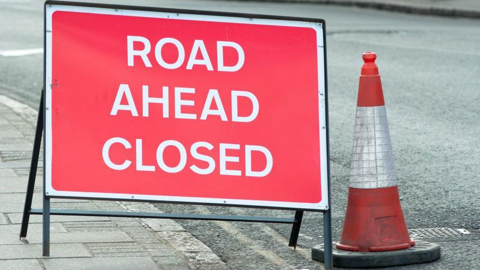 A road closed sign on a road a next to a bollard