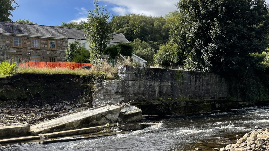 A wall that at the bottom of a garden that has collapsed into a river