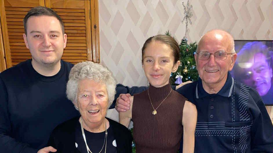 Hayley Morrison stands with her brother, gran and grandpa in front of a Christmas tree in a living room.