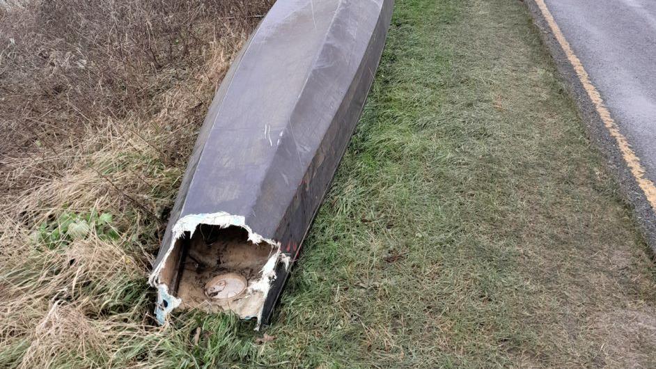 The wreckage of a dragon boat, upside down, on the side of a country road