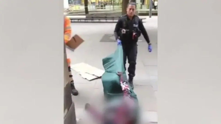 A still from a video showing a female police officer dragging a man in a sleeping bag across the ground