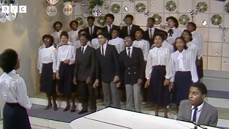 The women in the choir are wearing white blouses and skirts and the men, dark jackets and trousers and a white shirt.