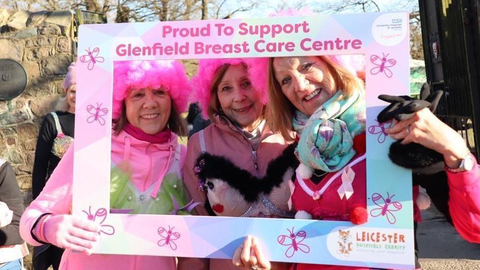 Walkers in pink wearing decorated bras pose with a frame