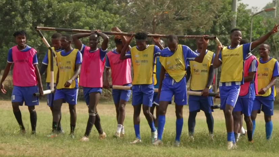 Talanta players moving goalposts during a training session in Nairobi, with nine players wearing purple or yellow bibs carrying the goal frame between them