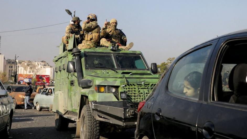 Rebel fighters ride a military vehicle, after they seized the capital and announced that they had ousted President Bashar al-Assad