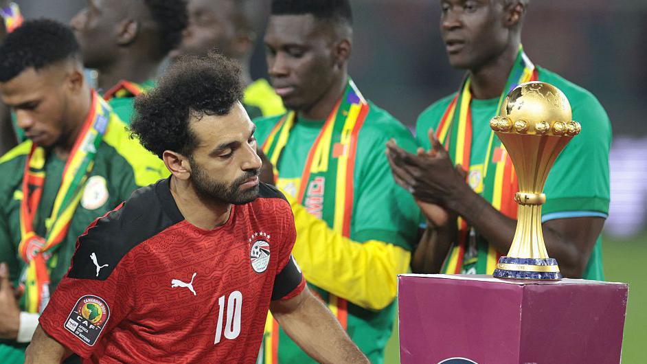 Salah walks past the Afcon trophy 