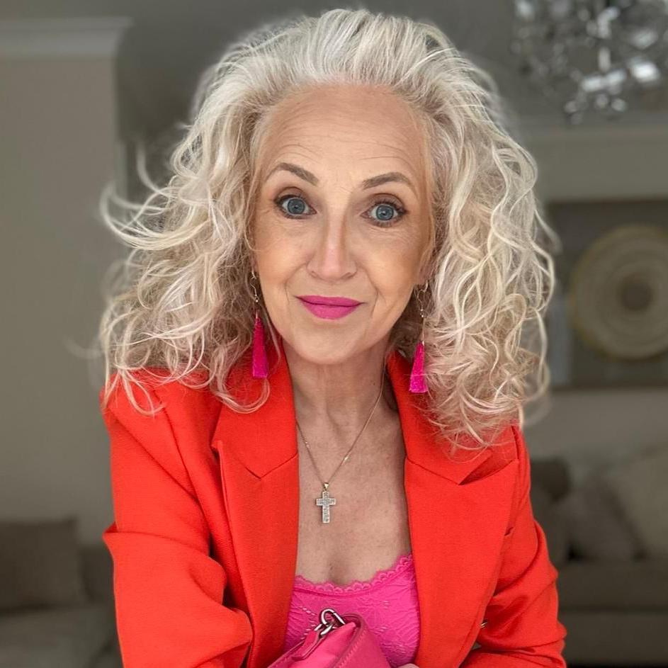 Mae gan Rhian wallt gwyn/llwyd hir a chyrliog. Mae hi'n gwisgo clustlysau pink hir gyda siaced coch.