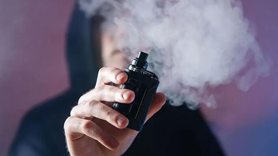 A person in a hoodie smoking a vape