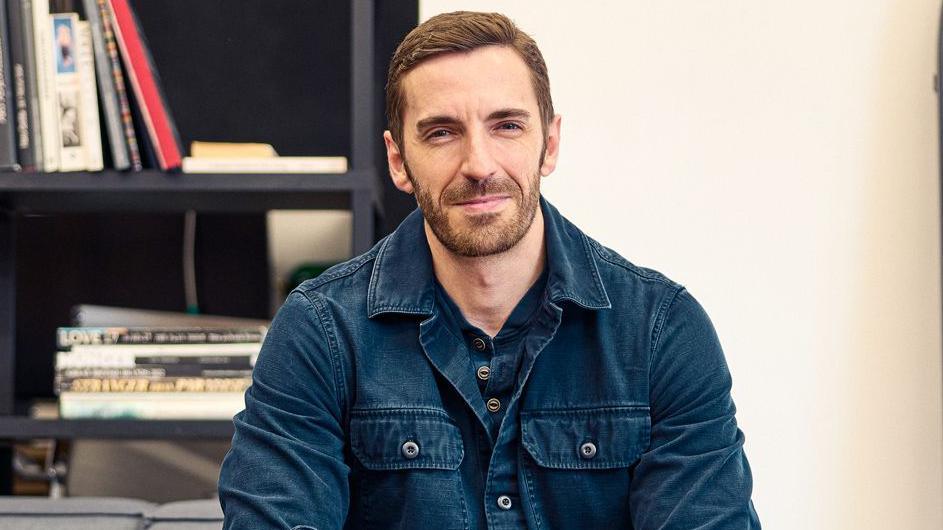 Ian Wharton, wearing a denim jacket, has short brown hair and brown stubble.