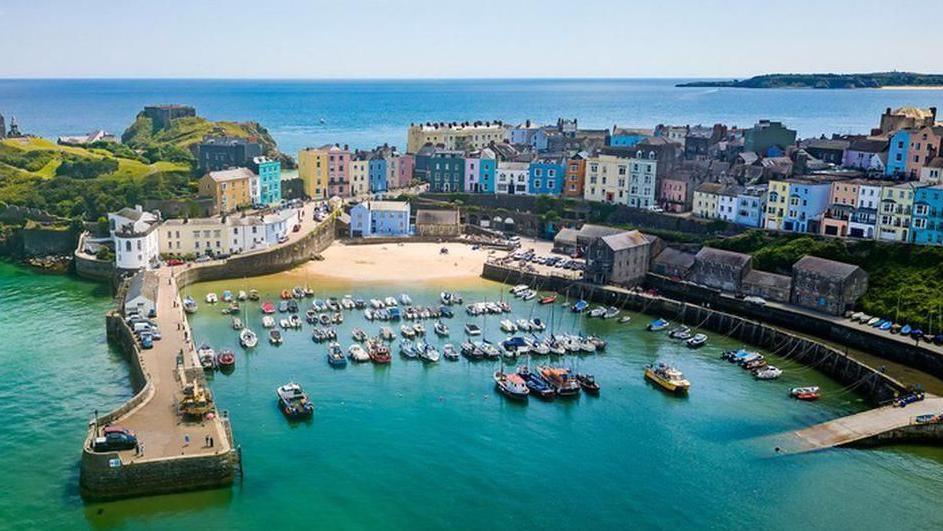 An aerial shot of Tenby harbour in Pembrokeshire, showing docked boats and colourful houses on the seafront.