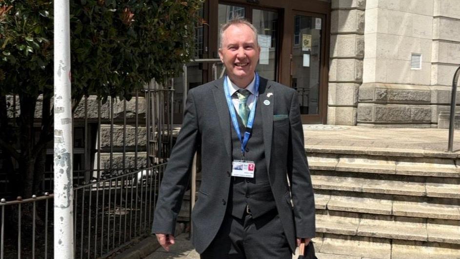 Councillor Robert Ford at County Hall in Maidstone. He is smiling and wearing a blue tie, white shirt and black jacket.