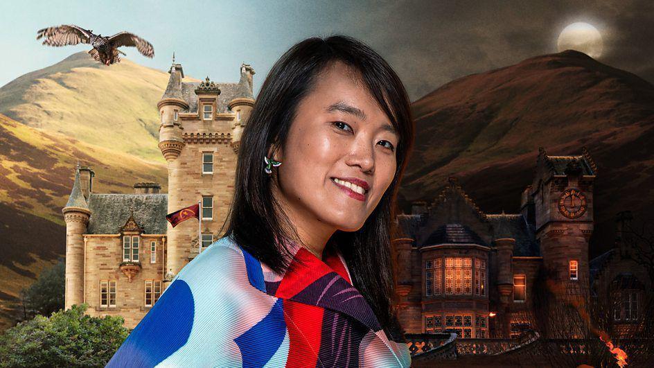 A publicity head-and-shoulders photo of Yin, a woman with shoulder-length dark hair and wearing a multicoloured shirt. Behind her is the traitors castle.