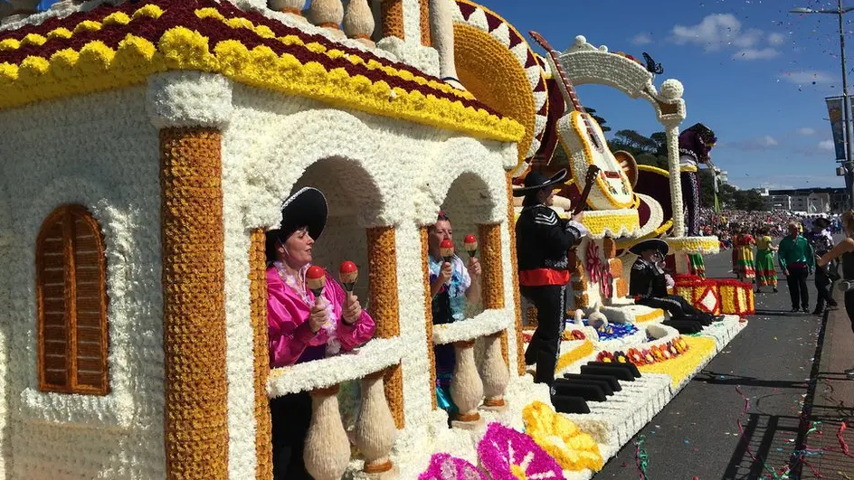 People performing on a florally decorated float on a parade.