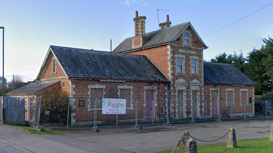 A derelict pub with fencing around it and the name Prince of Wales on a sign on its front.