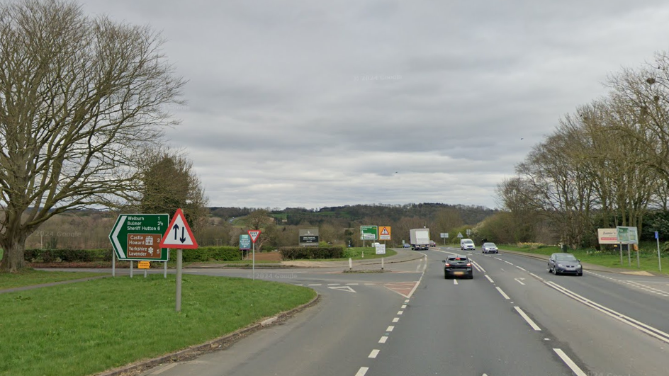 Cars travel along a main road, with a junction to the left with signs for Welburn and Castle Howard