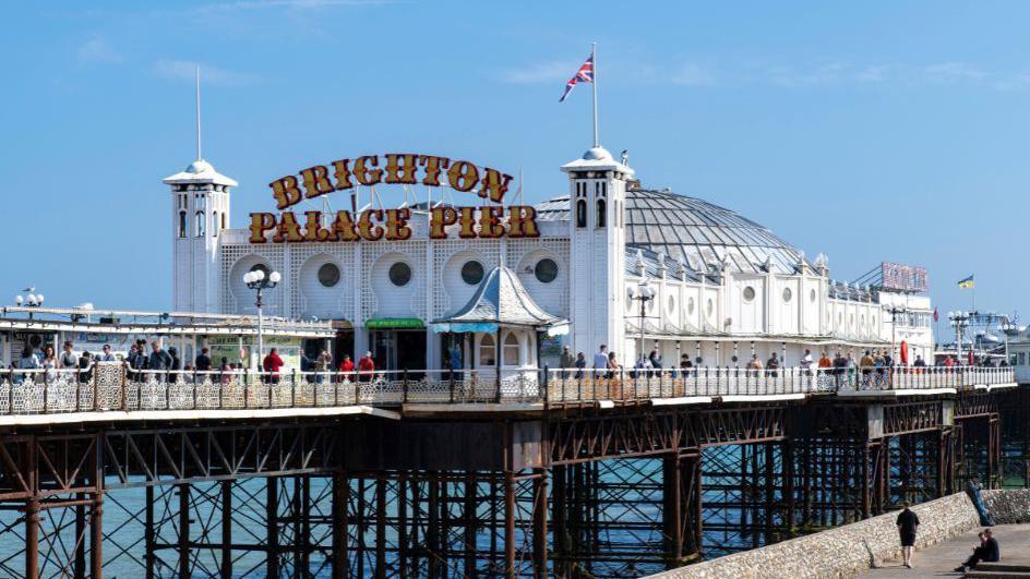 The front of Brighton Palace Pier. There are blue skies and people walking on the pier.