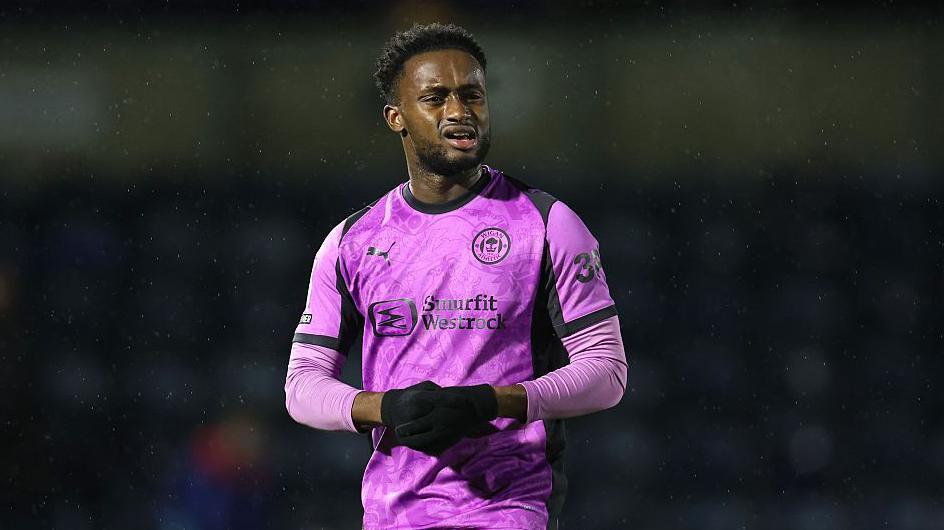 Steven Sessegnon looks on wearing Wigan's purple changed kit, and black gloves