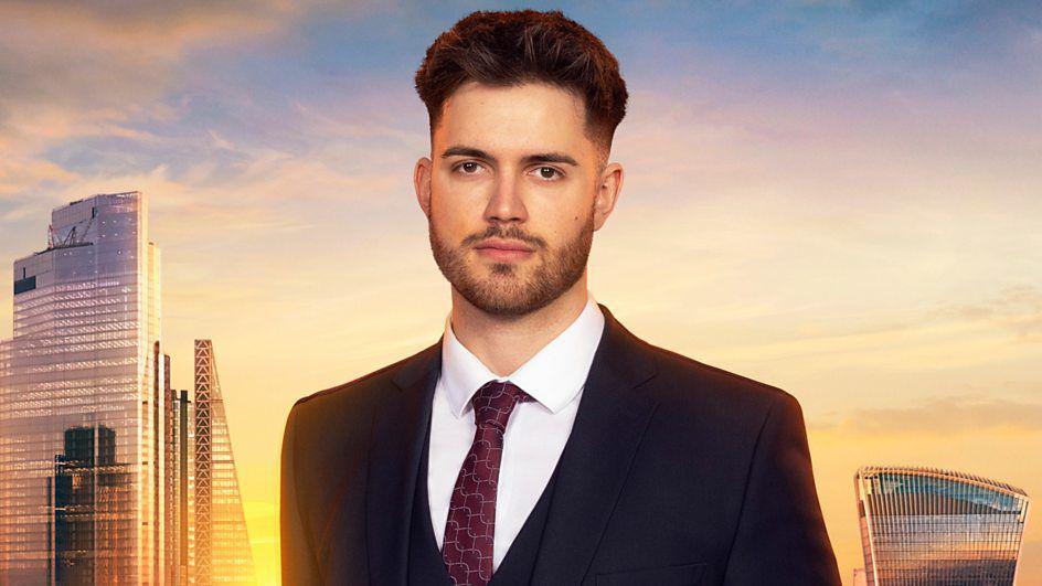 A man with dark hair and a short beard stands in front of the London skyline at sunset.