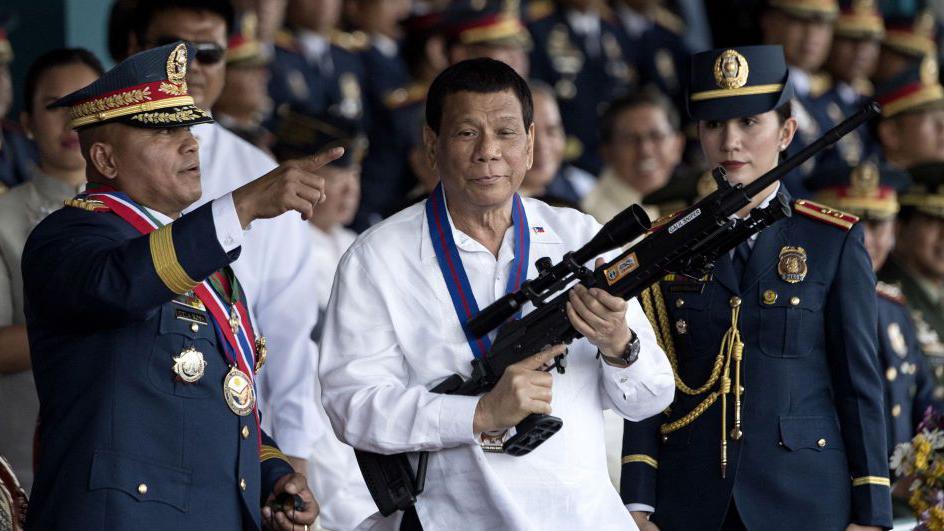 Former Philippine President Rodrigo Duterte (centre) holds a Galil sniper rifle with outgoing Philippine National Police chief Ronald dela Rosa (L) during the change of command ceremony in Manila on 19 April, 2018