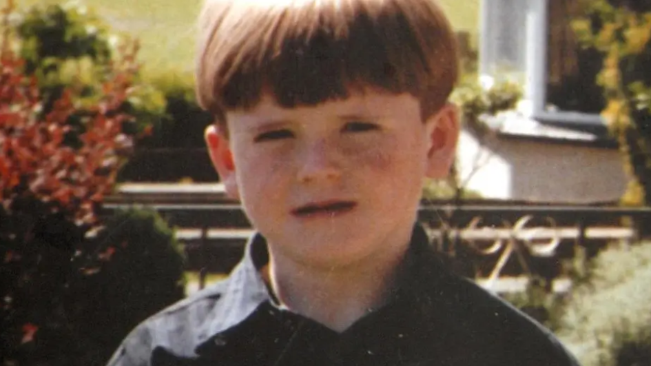 A young boy standing in a garden looking at the camera