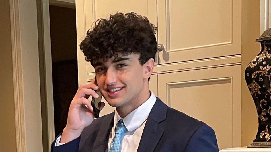 Kareem Badawi, smiling at the camera, wearing a dark blazer, white shirt and light blue tie, holding a mobile to his right ear. Image cropped to shoulders.